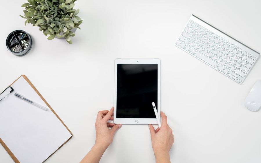 Hände bedienen ein Tablet auf einem aufgeräumten Schreibtisch